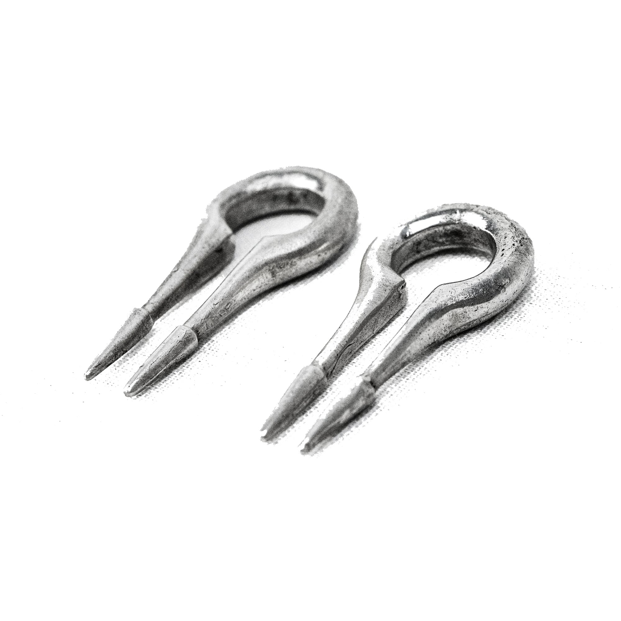 Close-up view of two CALYPSO Minimalist Keyhole Ear Weights in 925 Silver by Kaya Movement, each in a 2 gauge size. They feature a narrow, elongated U shape with two pointed prongs at the ends. The weights have a slightly rough, worn surface and are placed against a plain white background, resembling futuristic jewelry designed for stretched ears.